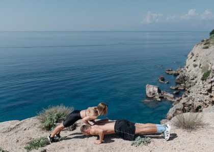 A couple performs a partner workout on a scenic cliffside, overlooking the ocean.