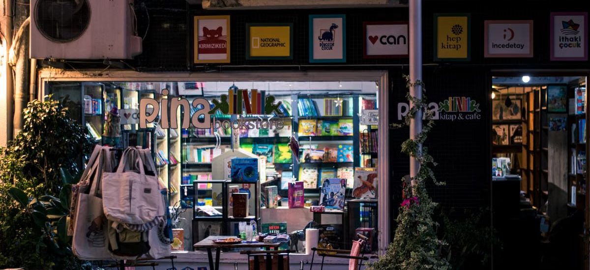 Charming nighttime bookstore and cafe scene, inviting ambiance with outdoor seating and books on display.